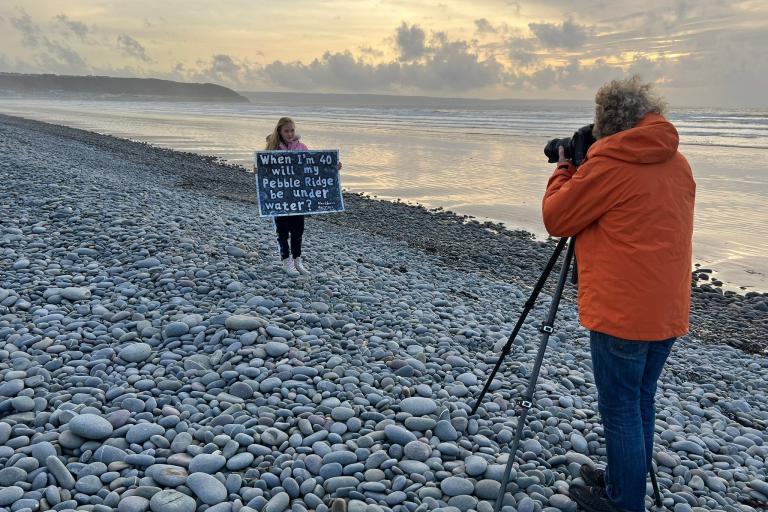 Man taking photograph of girl holding a sign on beach