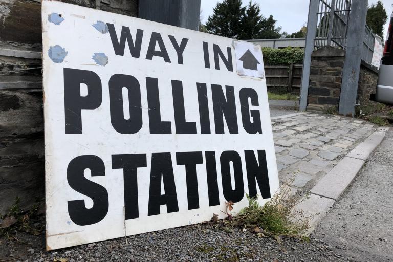 A polling station sign resting against a wall