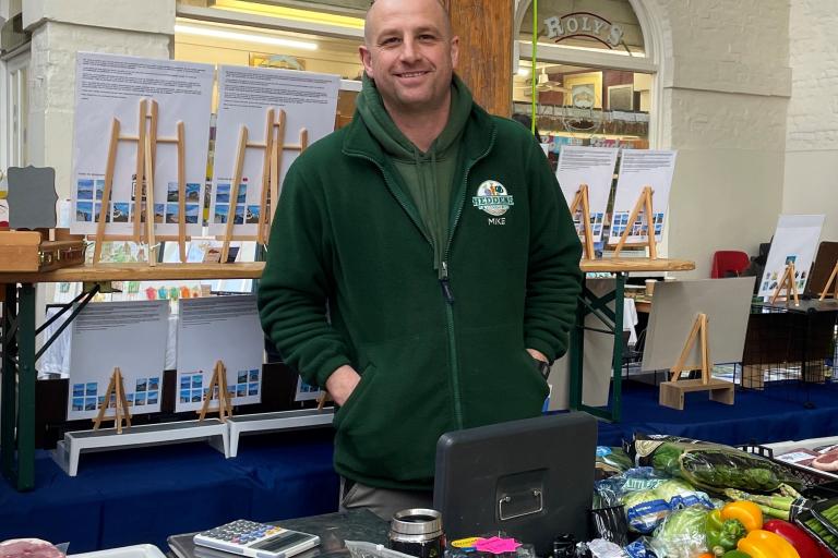 Man from Heddons smiling behind a stand of produce