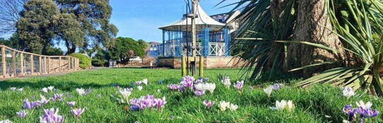 A park with a bed of flowers, trees and a gazebo